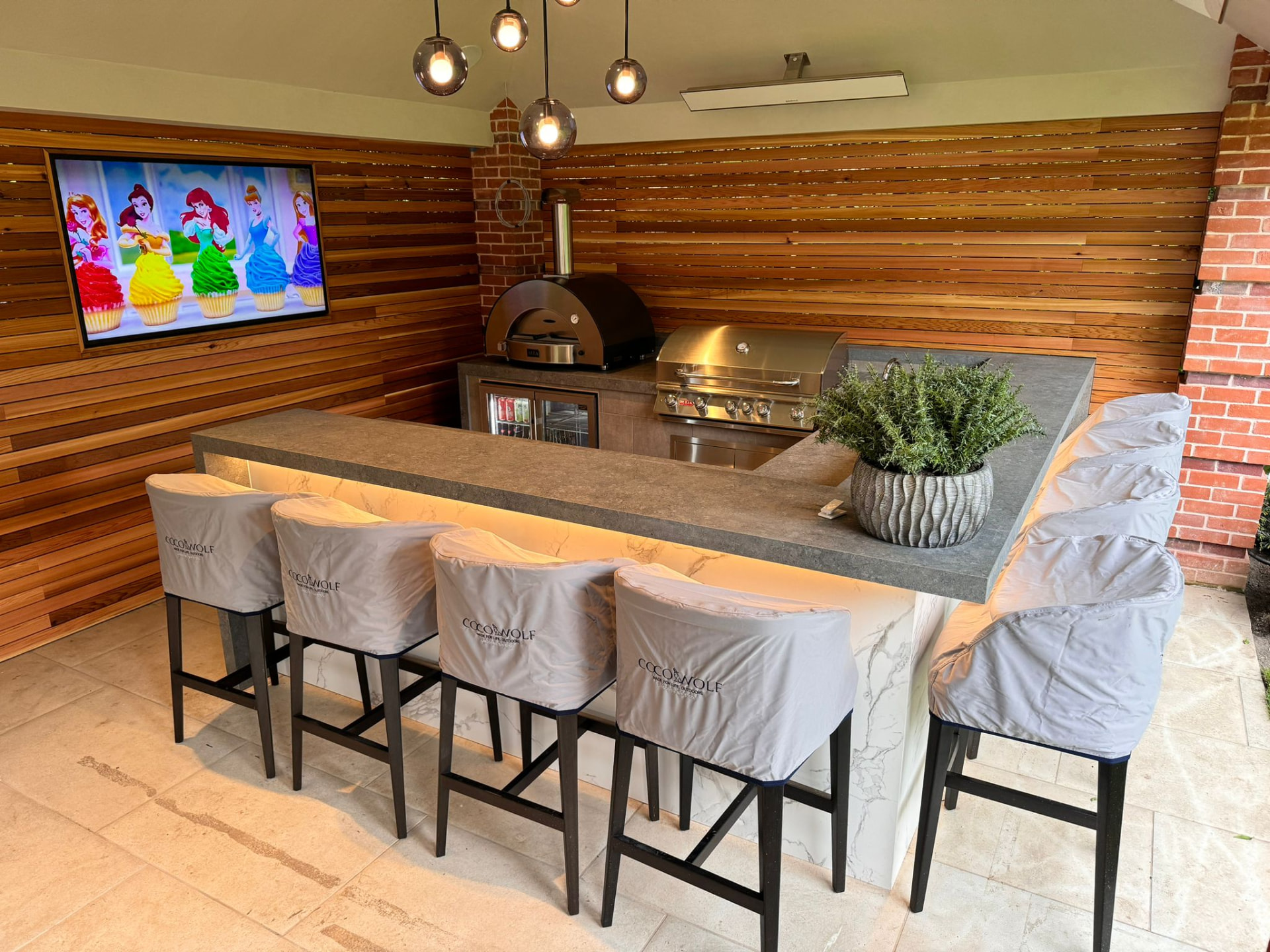 Covered outdoor kitchen with stone bar, grill, pizza oven and bar seating